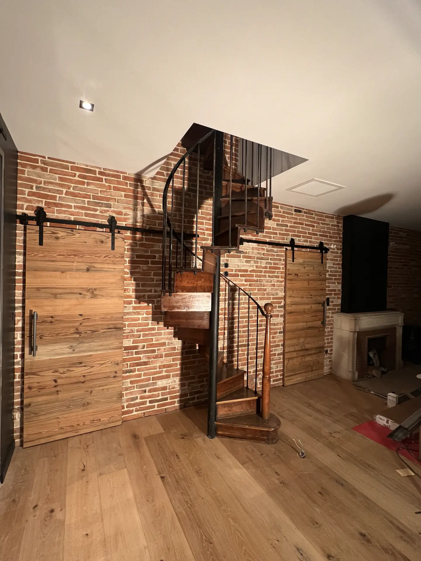 Escalier hélicoïdal métallique devant un mur de briques apparentes dans un logement rénové à Vienne