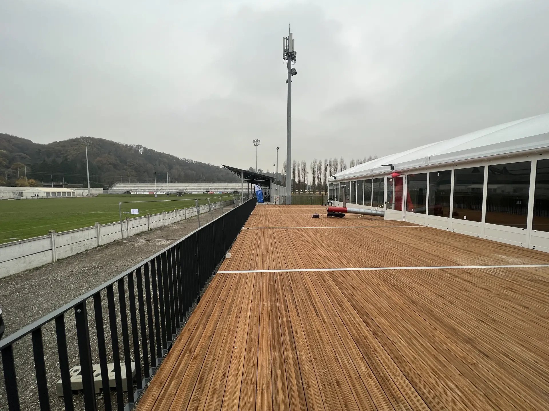 Terrasse en bois avec garde-corps métallique longeant un terrain de rugby à Vienne